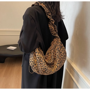 Détail d'un sac bandoulière en toile léopard porté avec un manteau noir élégant
