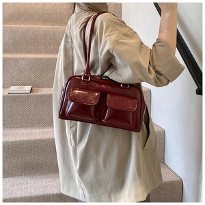 Détail d'un sac à main en cuir verni bordeaux avec doubles poches porté par un mannequin