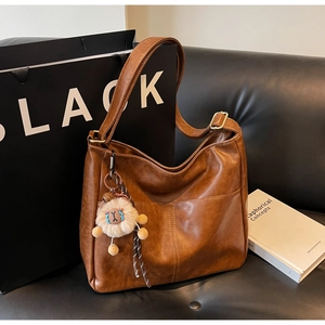 Close-up of brown pebbled leather tote bag with alpaca plush charm on a sofa