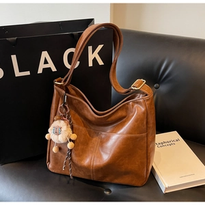 Brown vintage faux leather tote bag on black leather sofa with a cute sheep plush charm