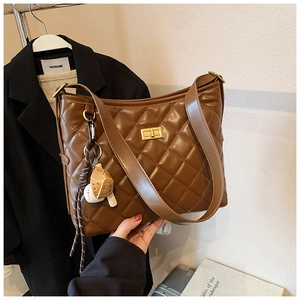 Détail d'un sac seau matelassé marron avec fermoir tournant doré et breloque baseball