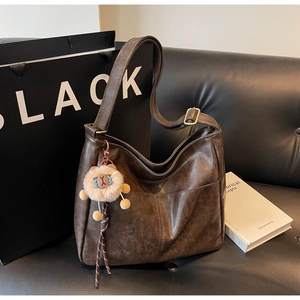 Detail of dark brown leather tote bag featuring a plush lion charm and wide strap on a sofa