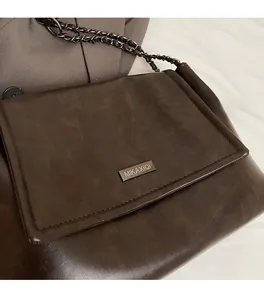Détail du sac bandoulière marron mat avec logo métallique et bandoulière chaîne