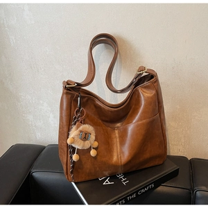Detail of a brown leather tote bag with a cute lion charm and vertical stitching details