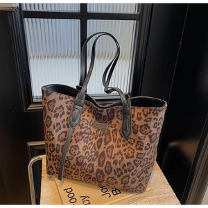 Detail of leopard print tote bag with black straps and brand logo on a textured surface