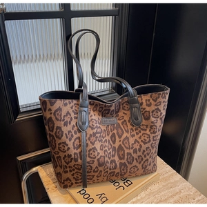 Close-up of leopard print tote bag with black leather handles and logo patch detail
