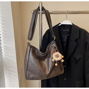 Detail of dark brown hobo bag with vintage texture and plush lion charm on a hanger