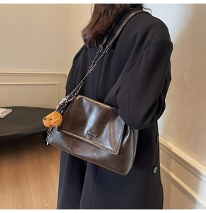 Détail du sac chaîne en cuir brillant marron foncé avec logo et breloque ours
