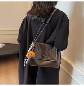 Détail du sac à bandoulière en cuir marron foncé avec chaîne dorée et bijou ours