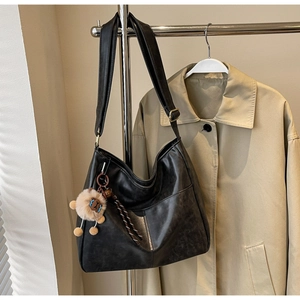 Detail of a black leather tote bag with a lion plush charm on a metal hanger with trench coat