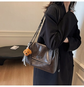 Détail macro du sac vintage marron brillant avec chaîne en métal et breloque ours en peluche
