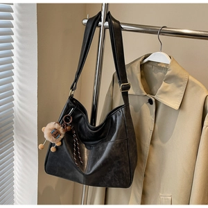 Detail view of large black retro hobo bag in textured faux leather with lion charm