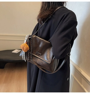 Détail du sac bandoulière rétro marron foncé avec chaîne métallique et breloque ours