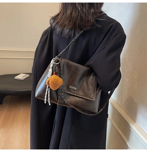 Détail d'un sac porté épaule en cuir marron avec chaîne dorée et breloque en peluche