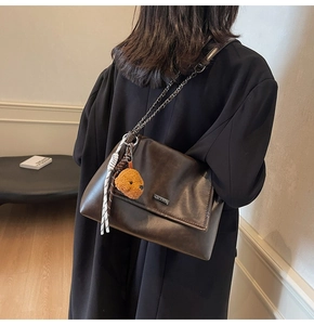 Détail du sac bandoulière en cuir marron foncé avec chaîne et pendentif chien en peluche