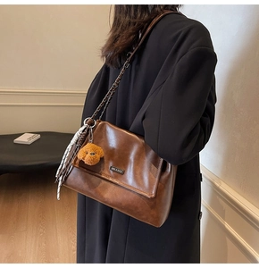 Détail du sac en cuir marron avec bandoulière chaîne, peluche ours et ruban en soie