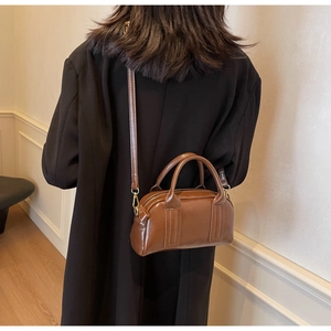 Rückansicht eines Models im schwarzen Mantel mit dunkelbrauner Boston Tasche und Golddetails
