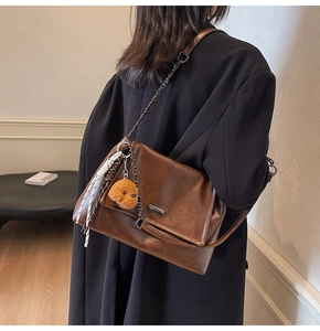 Gros plan du sac bandoulière vintage marron avec chaîne, breloque ours et foulard