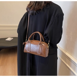 Braune glänzende Boston Tasche als Umhängetasche über einem schwarzen Herbstmantel