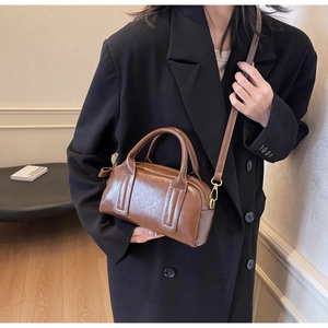 Borsa Boston vintage marrone con hardware dorato e tracolla su un blazer nero