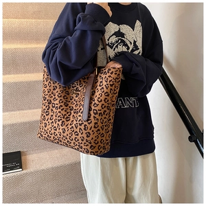 Close-up of leopard print tote bag featuring brown leather handles and a gold metal logo