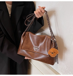 Détail du sac bandoulière en cuir marron avec bandoulière chaîne et charme de chien peluche