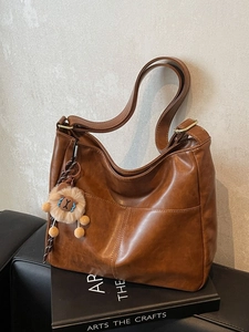 Brown vintage faux leather tote bag with lion plush charm on a black sofa