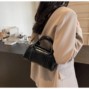 Dettaglio di una borsa Boston in pelle nera lucida su una modella in interni moderni