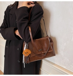 Détail d'un sac porté épaule marron vintage avec chaîne en métal et ours en peluche
