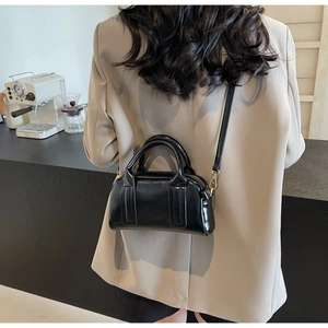 Rückansicht eines Models mit schwarzer Boston-Tasche aus glänzendem Leder und Goldteilen