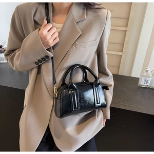 Detail der schwarzen Lackleder-Boston-Tasche mit goldenen Haken am beigen Anzug