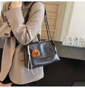 Détail d'un sac à épaule en cuir noir avec chaîne en métal et breloque chien peluche