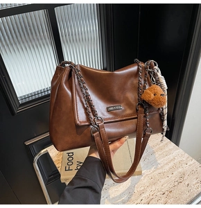 Détail du sac bandoulière marron avec logo en métal, chaîne et pendentif ours en peluche