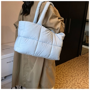Detail van een lichtblauwe gewatteerde tote bag met vierkante puffer-textuur en brede schouderband