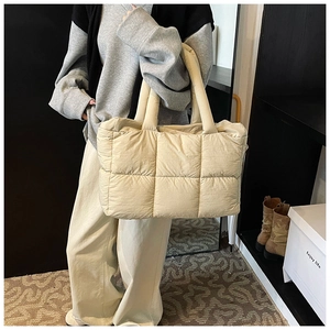 Detailed view of beige quilted puffer tote bag worn by a model in a minimalist setting