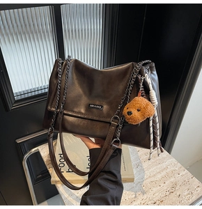 Détail d'un sac cabas en cuir marron foncé avec bandoulière chaîne et breloque ours