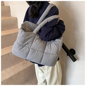 Detail van grijze gewatteerde nylon draagtas met brede schouderriem getoond op model