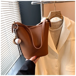 Detail of brown litchi pattern bucket bag with a mini baseball charm and strap
