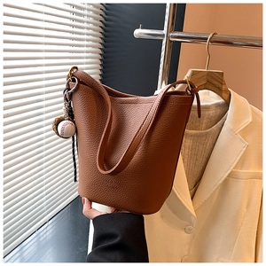 Detailed close-up of brown pebbled leather bucket bag with a creative baseball charm