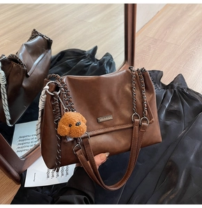 Détail d'un sac bandoulière en cuir marron avec chaîne en métal et pendentif chien en peluche