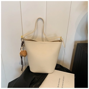 Detail of a creamy white bucket bag featuring litchi texture and a brown heart charm
