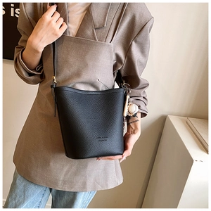 Detail of black lychee leather bucket bag with creative baseball charm and slim strap