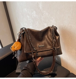 Détail du sac à bandoulière en cuir marron avec chaîne dorée et breloque ours