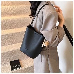 Detail of black lychee leather bucket bag featuring a baseball charm and woven rope