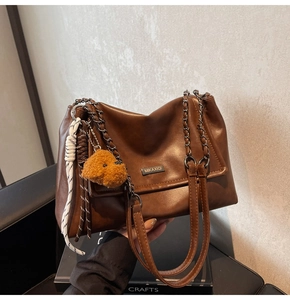 Détail d'un sac bandoulière en cuir marron avec chaîne en métal et breloque ours