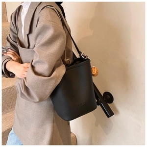 Detail of black lychee grain leather bucket bag with brand logo and brown sphere charm