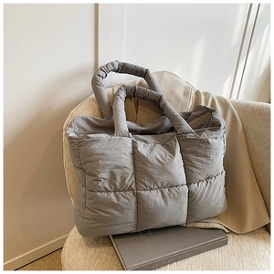 Detailweergave van de grijze gewatteerde puffer tote bag op een bank met natuurlijk licht