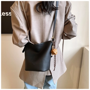 Detail view of black lychee grain leather bucket bag with a cute brown dog bag charm
