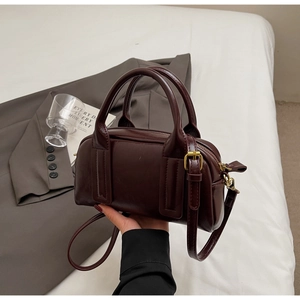 Detail der tief rotbraunen Boston Tasche mit goldener Hardware und Schultergurt
