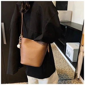 Detail view of caramel pebbled leather bucket bag with a baseball charm and shoulder strap